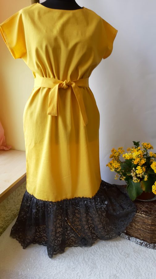 Dzeltena lina kleita ar tumši pelēku mežģīni.